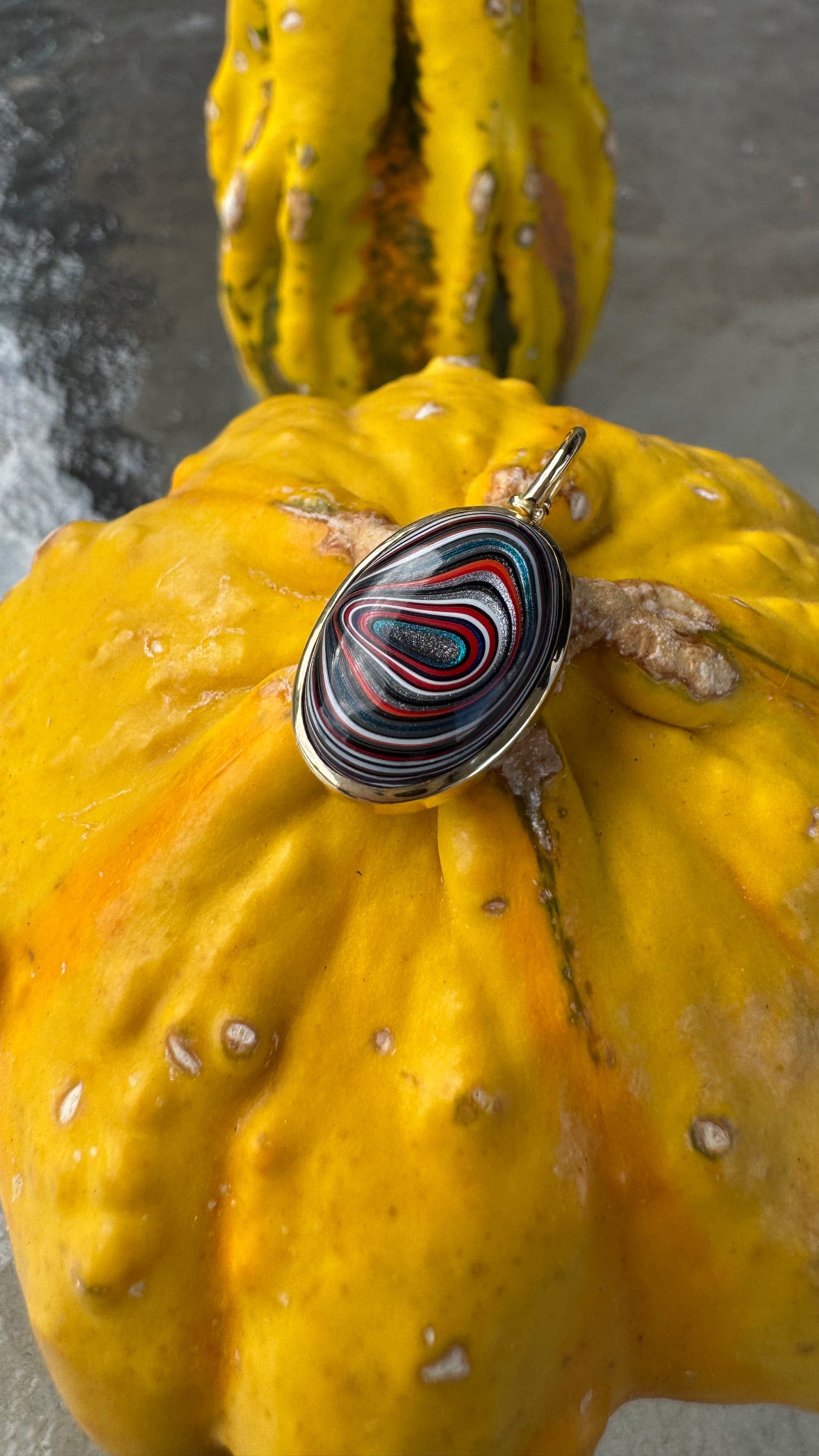 Colorful patterned fordite pendant on a yellow squash