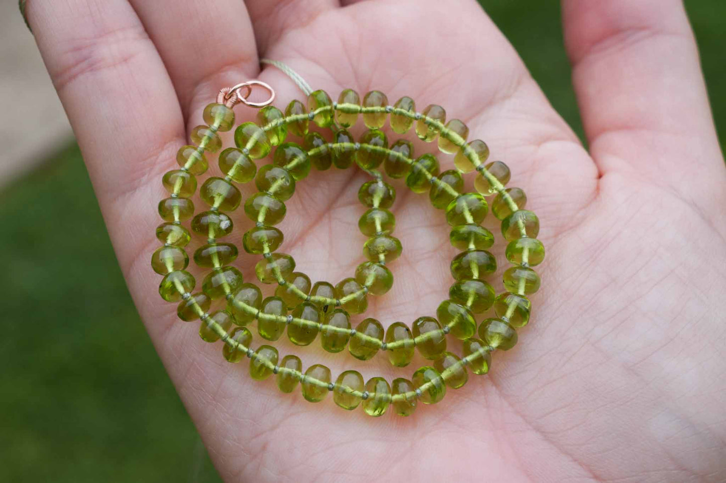 Green bead necklace held in a hand with a blurred green background