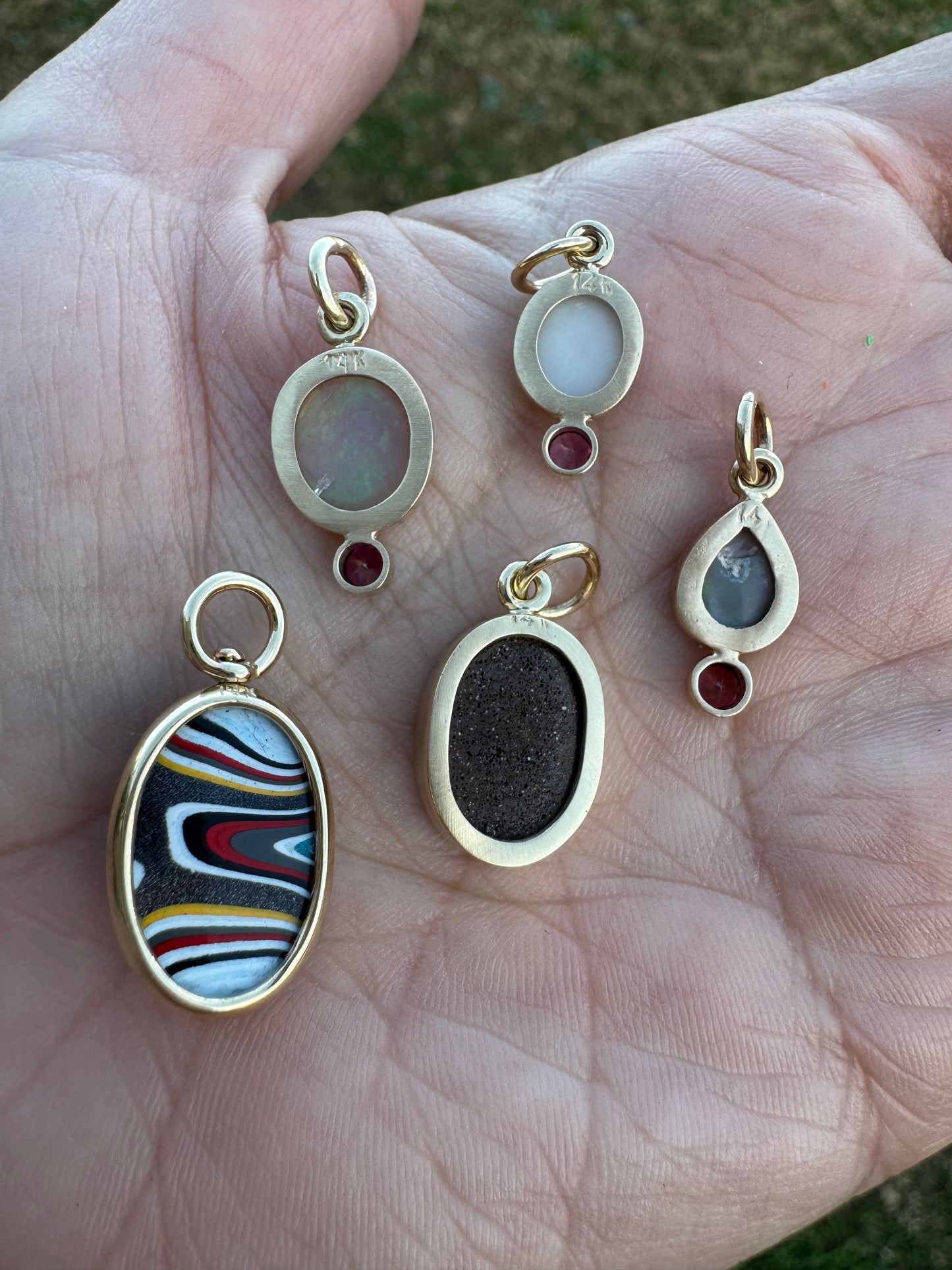 Gold pendants with various colored stones held in a hand.