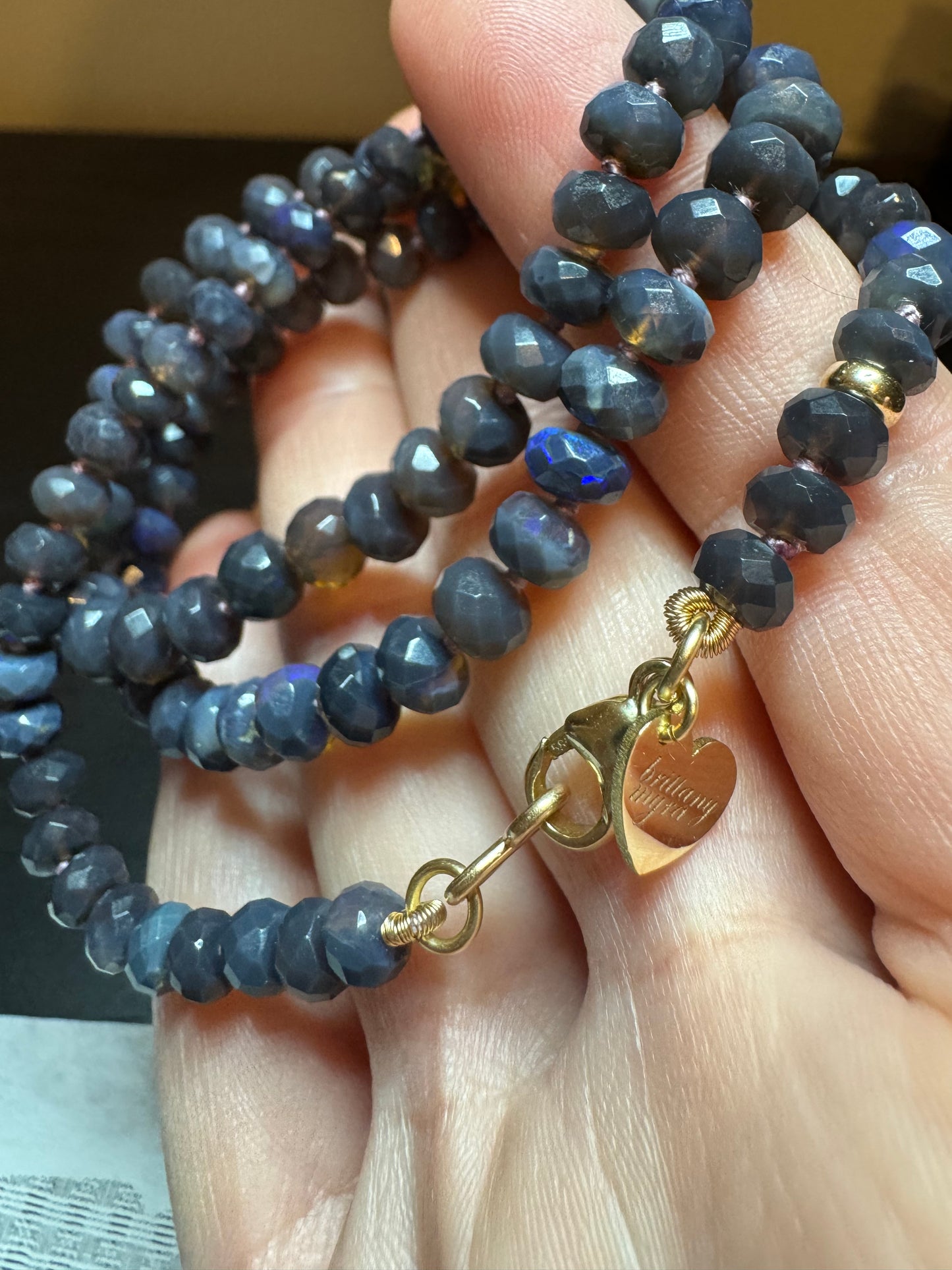Close-up of a beaded necklace with a gold clasp held by a hand.