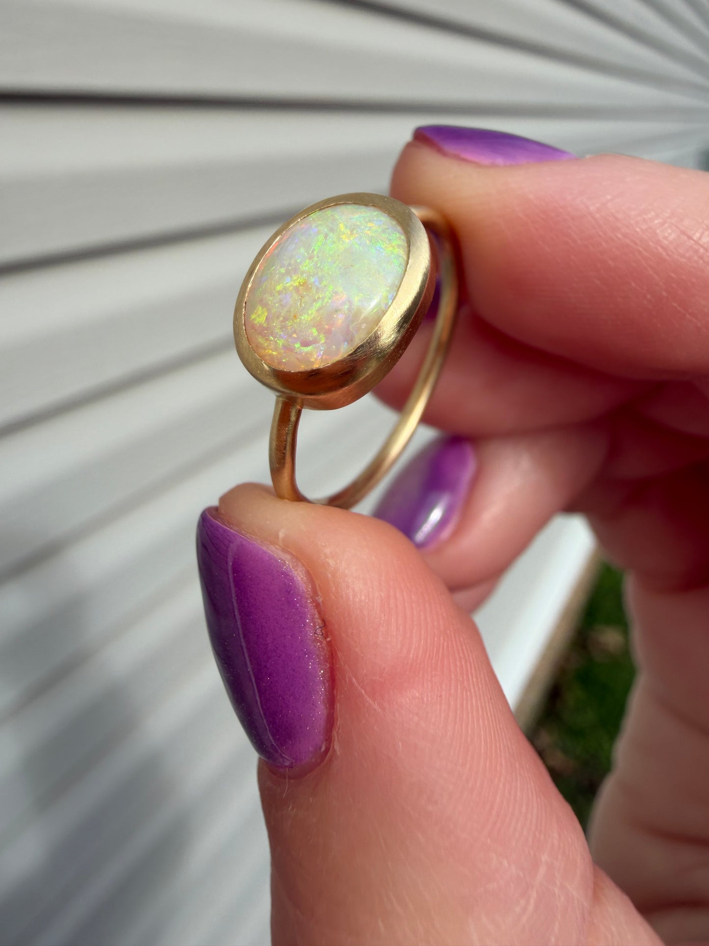 Gold ring with an opal stone held between fingers with purple nail polish.