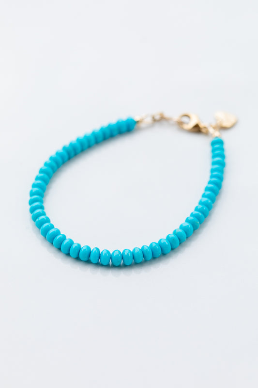 Turquoise beaded bracelet with a gold clasp on a light blue background