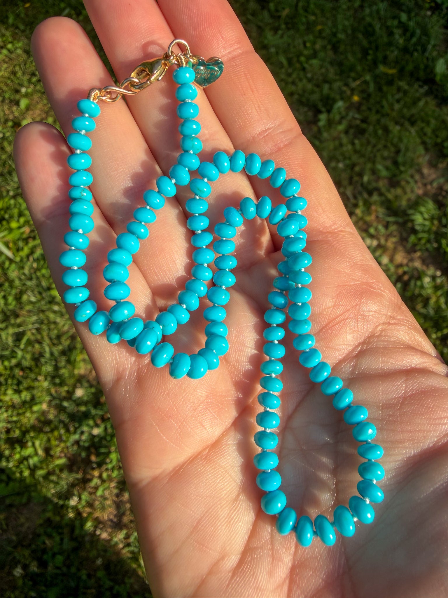 Turquoise beaded necklace held in a hand with grass in the background