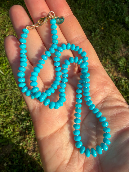 Turquoise beaded necklace held in a hand with grass in the background