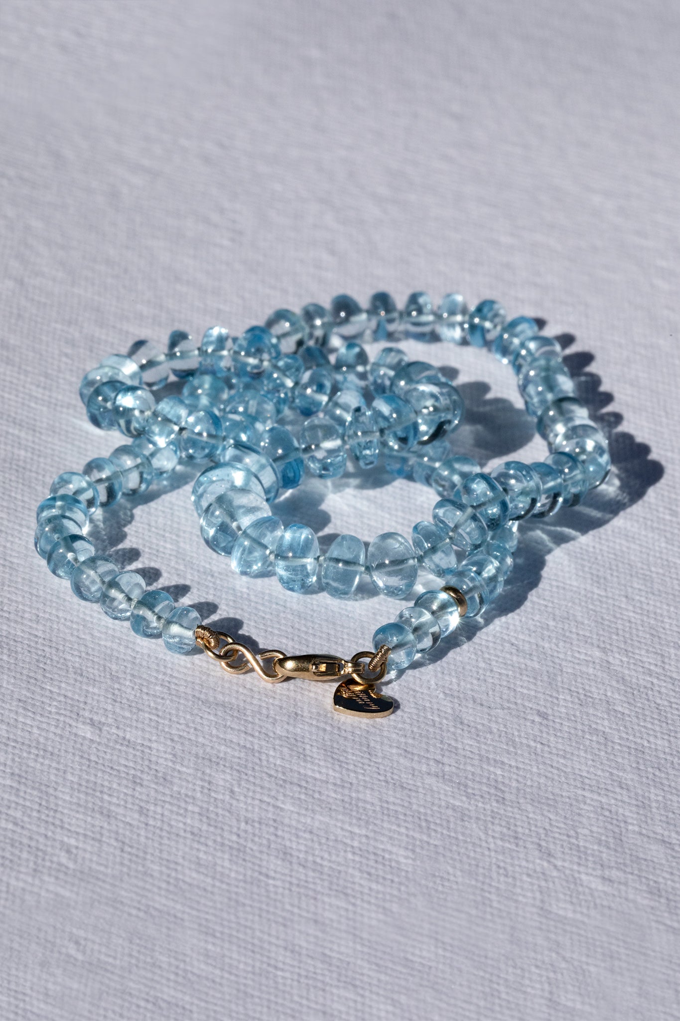 Blue beaded necklace with a gold clasp on a light gray background
