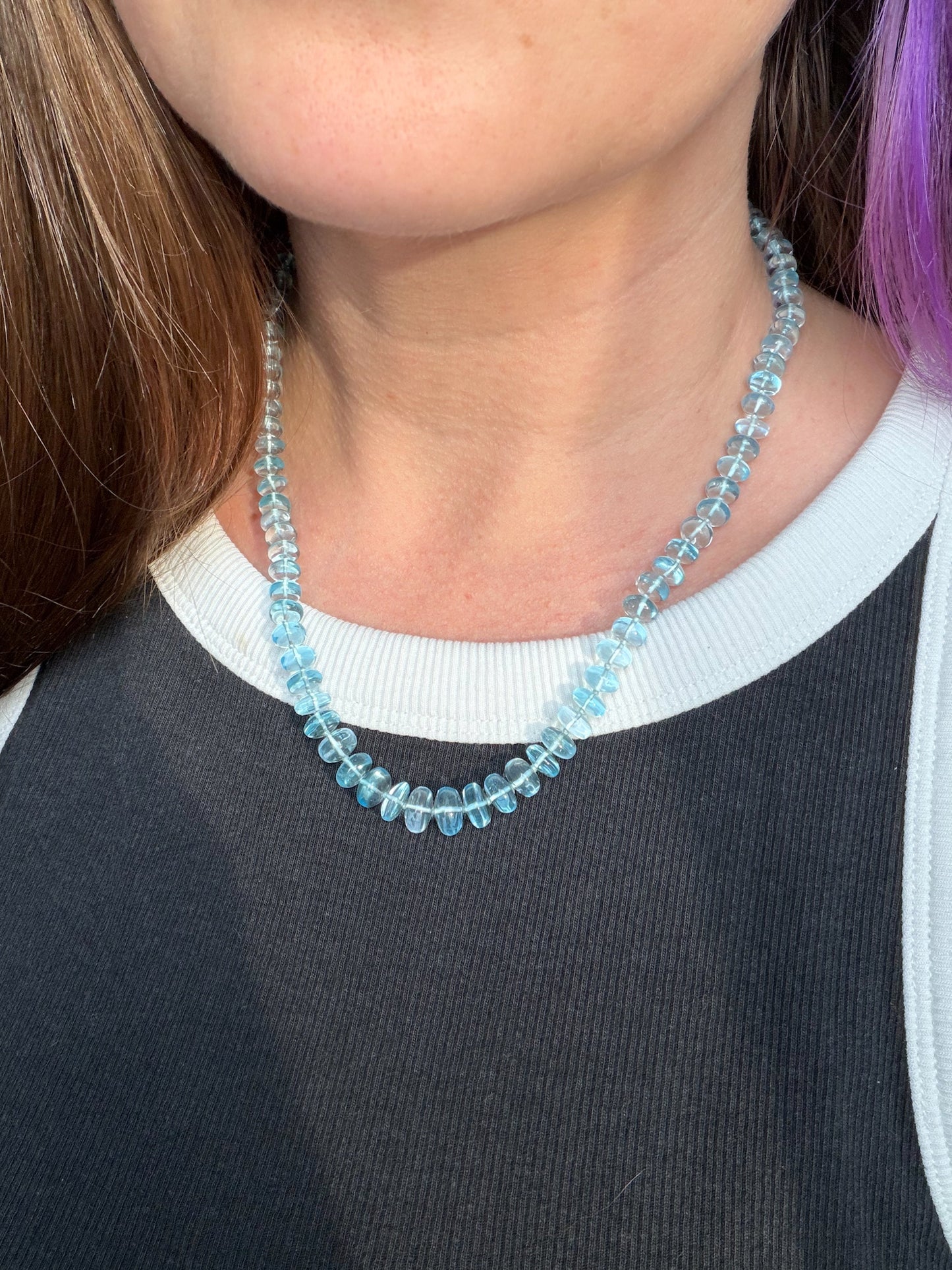 Person wearing a blue beaded necklace with a blurred background