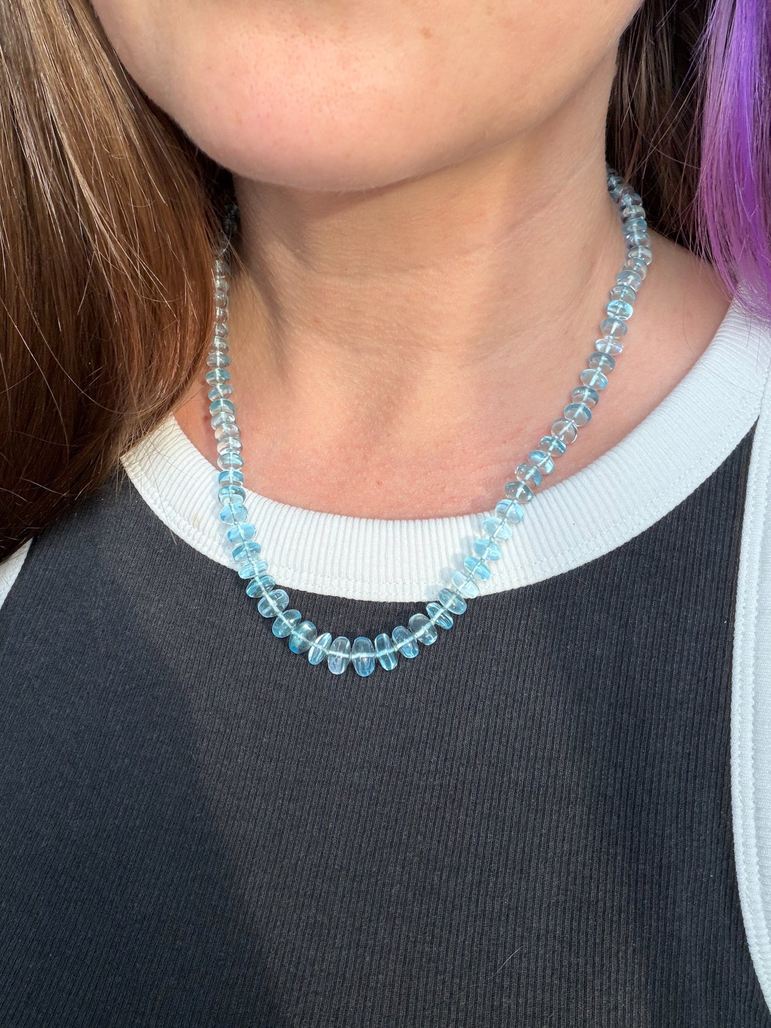 Person wearing a blue beaded necklace with a blurred background
