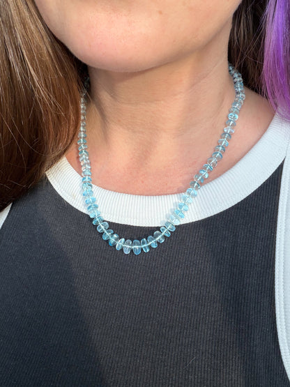 Person wearing a blue beaded necklace with a blurred background