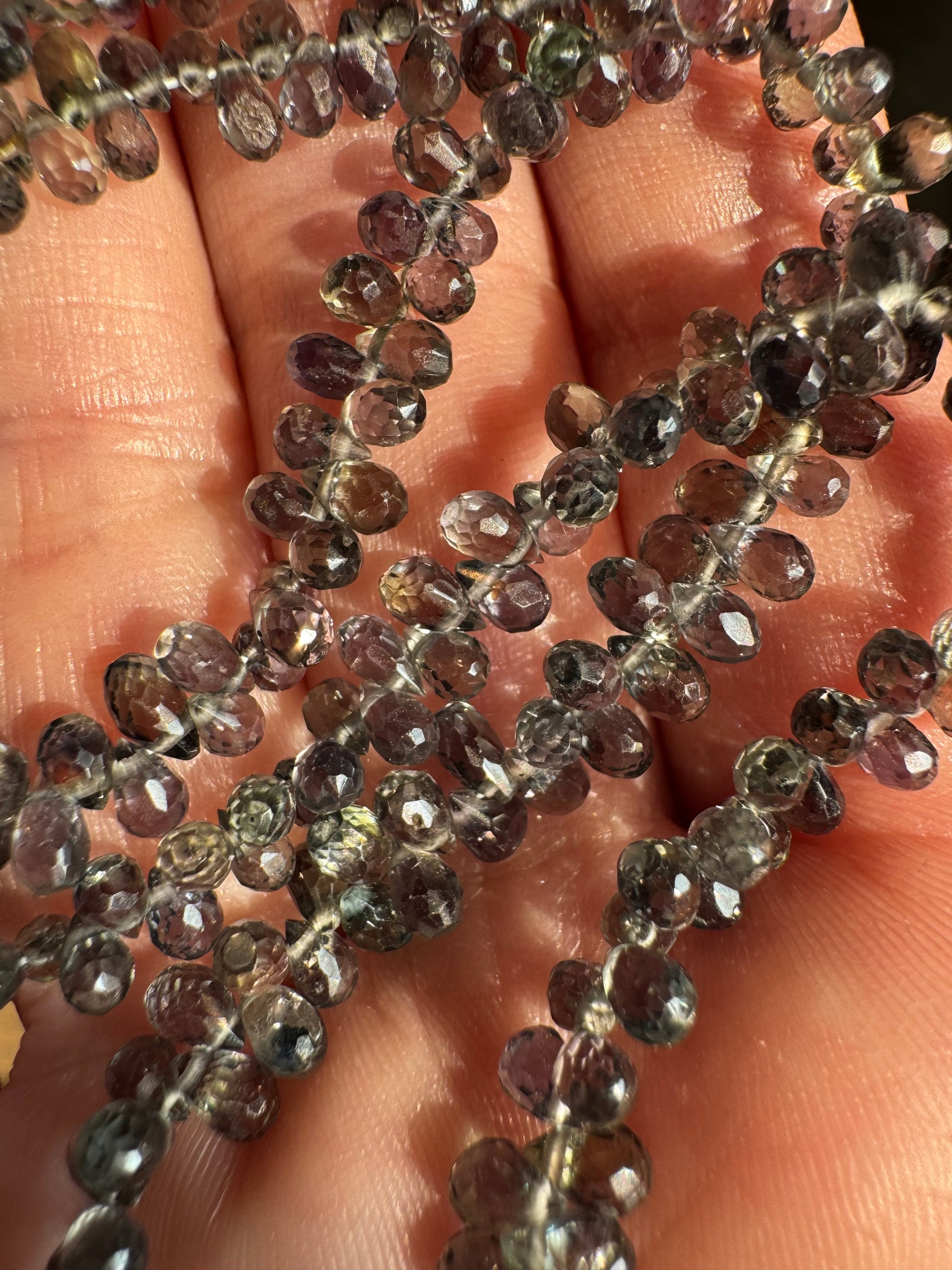 Close-up of a string of small, faceted gemstones held between fingers.