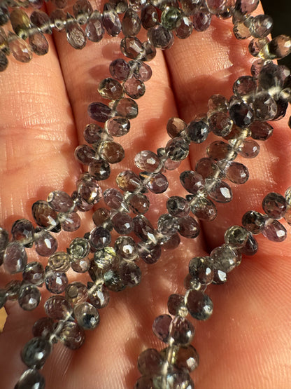Close-up of a string of small, faceted gemstones held between fingers.