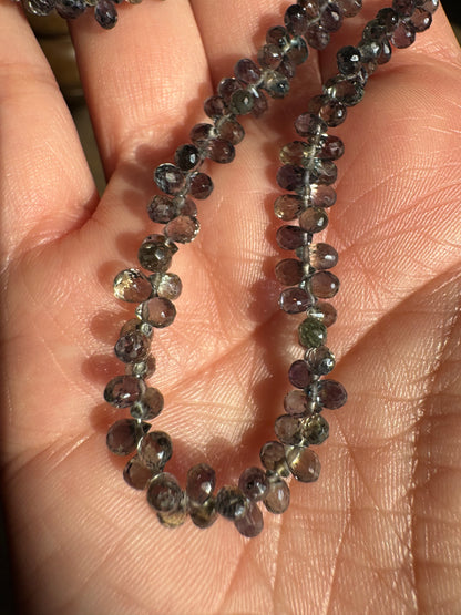 Close-up of a string of small, faceted gemstones held in a hand.