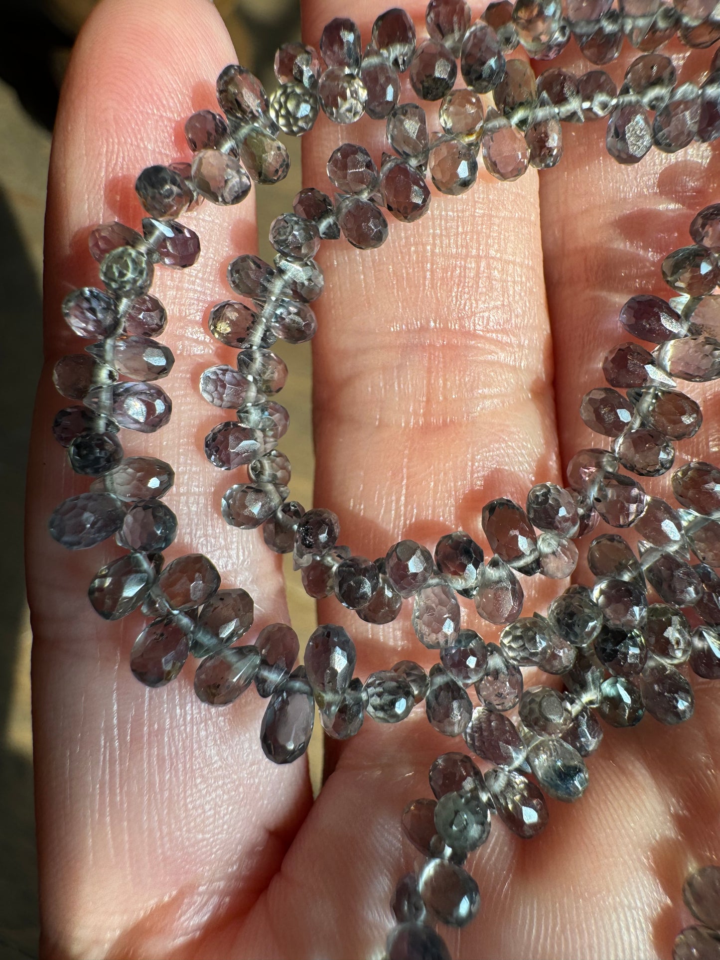Close-up of a hand holding a string of small, faceted gemstones.