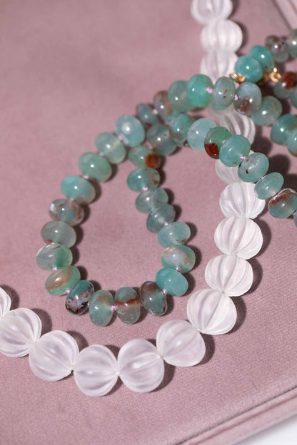 Two beaded bracelets, one with greenish-blue beads and the other with white beads, on a pink surface.Carved Quartz Pumpkins 14k Gold Knotted Candy Bead Necklace
