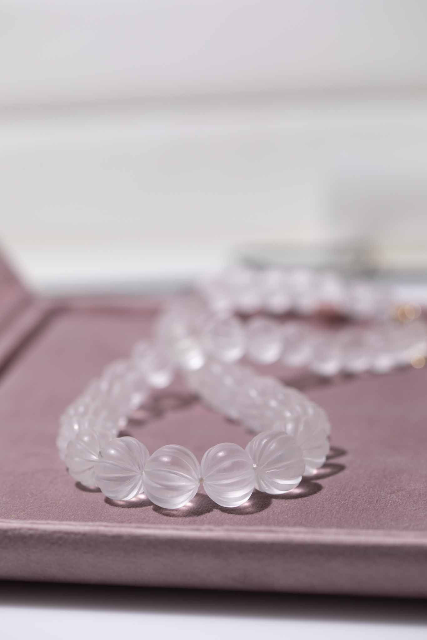 Set of clear beaded necklace on a pink surface with a blurred background