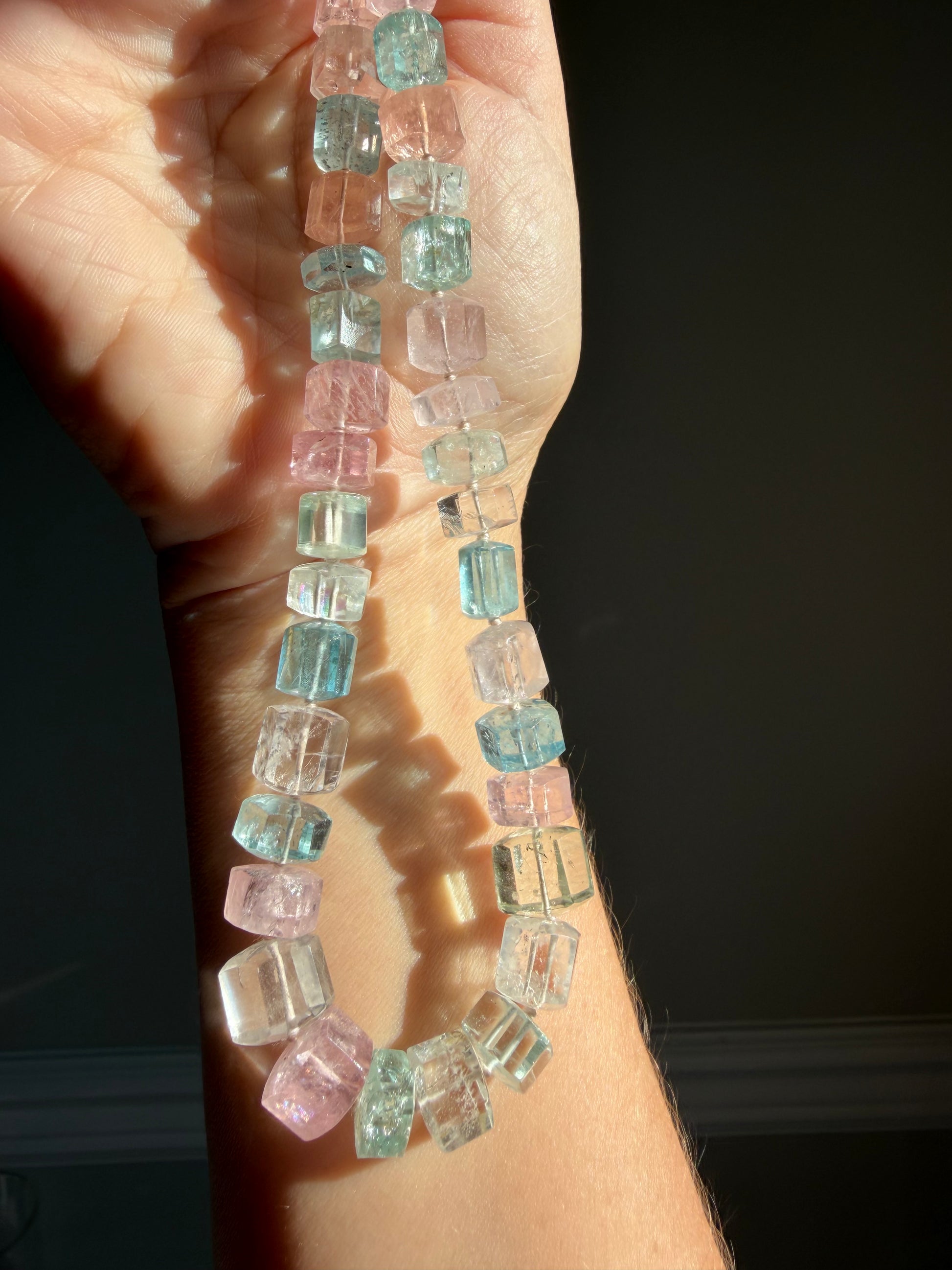 Close-up of hand-knotted aquamarine gemstones showing pink, blue, green, and peach beryl crystals