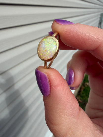 Hand holding a gold ring with an opal stone against a neutral background