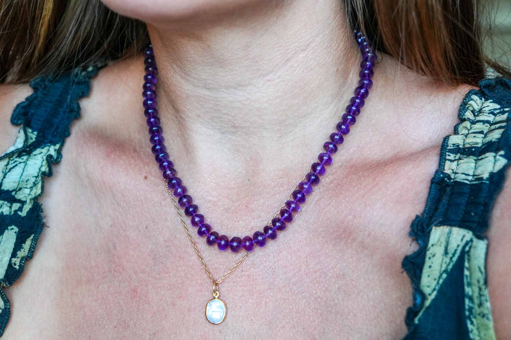 Close-up of a person wearing a purple beaded necklace with a gold pendant.