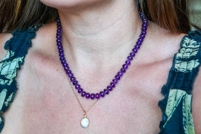 Close-up of a person wearing a purple beaded necklace with a gold pendant.