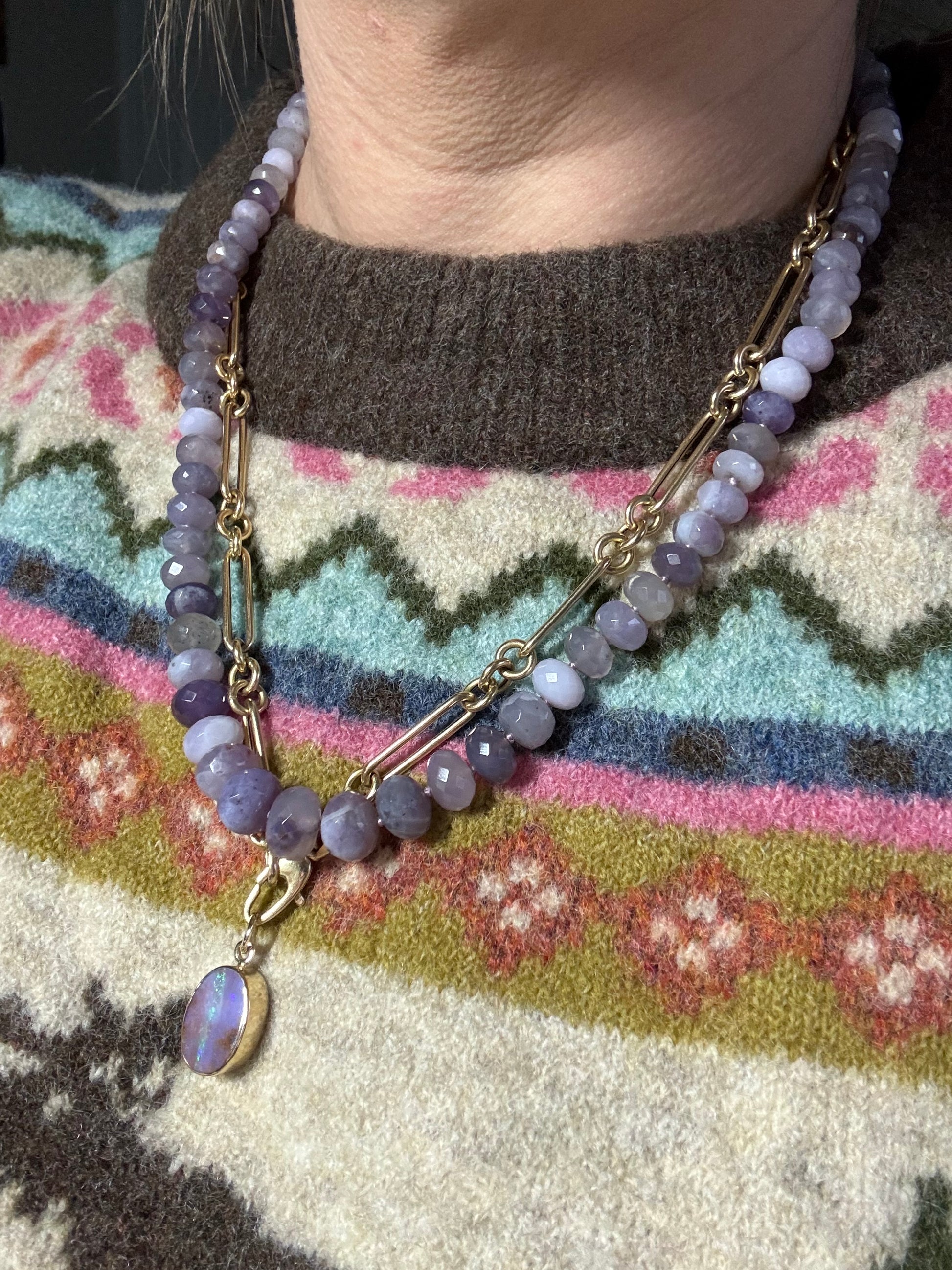 Bracelet with purple beads and gold chain on a patterned fabric background