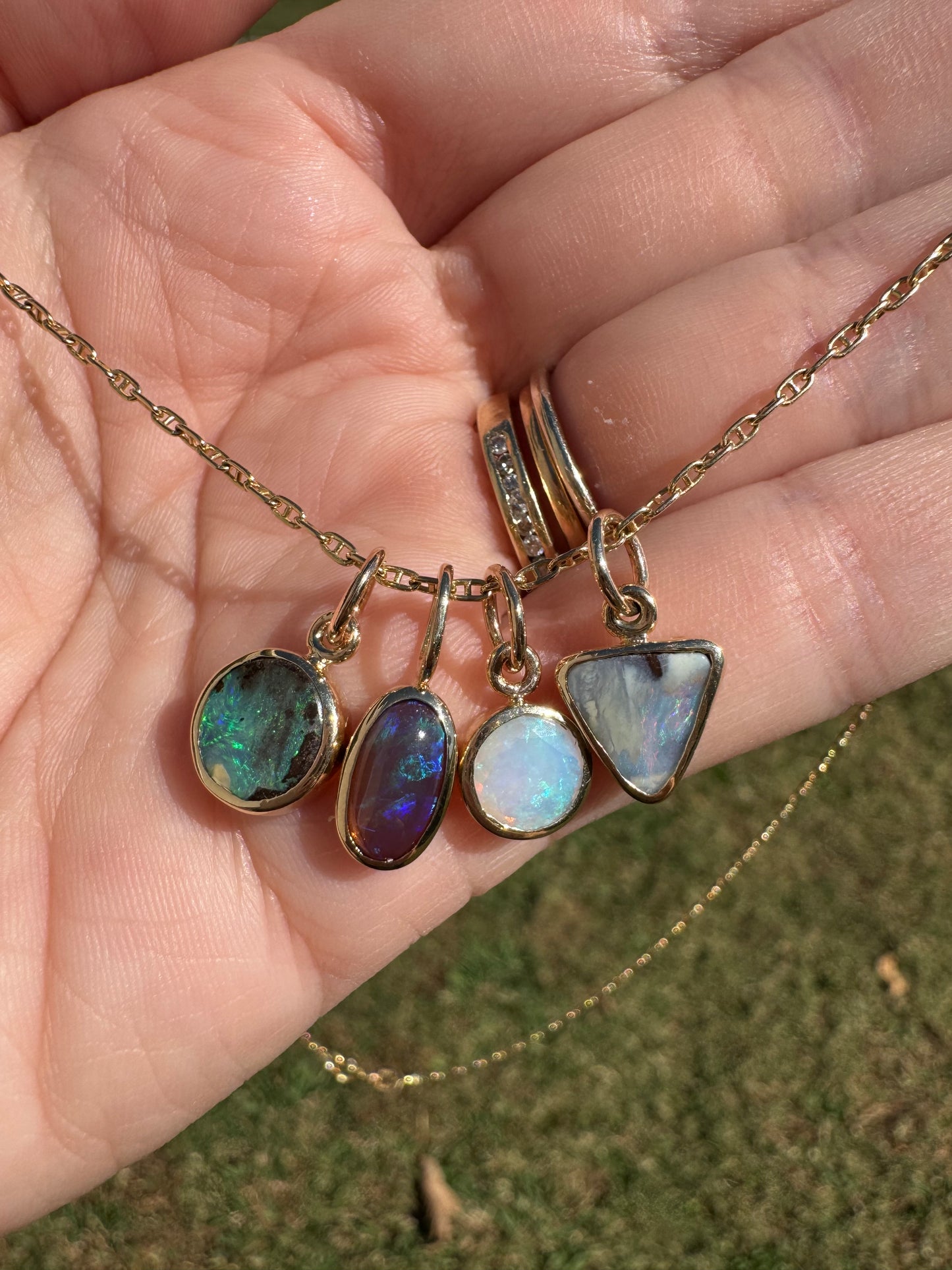 Gold necklace with opal pendants held in a hand against a grassy background