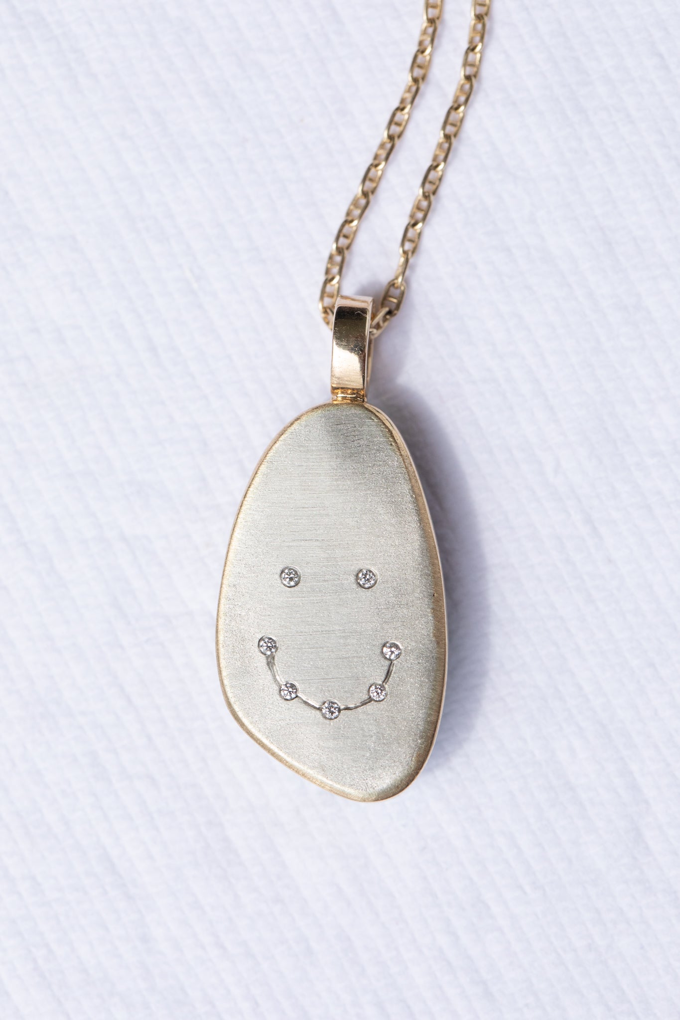 Necklace with a pendant featuring a smiley face diamond design on a light background
