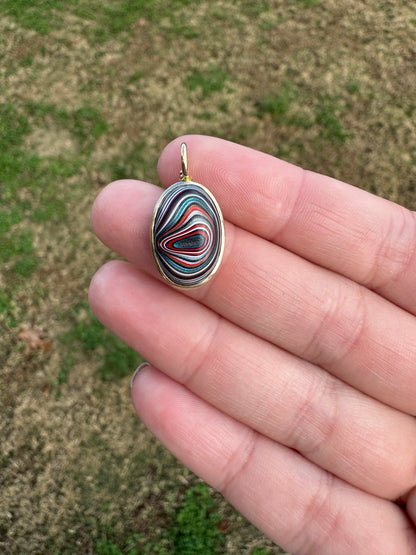 Colorful FORDITE CHARM held between fingers against a blurred natural background