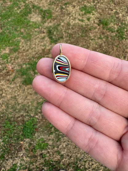 Hand holding a fordite charm with a multicolored design against a grassy background
