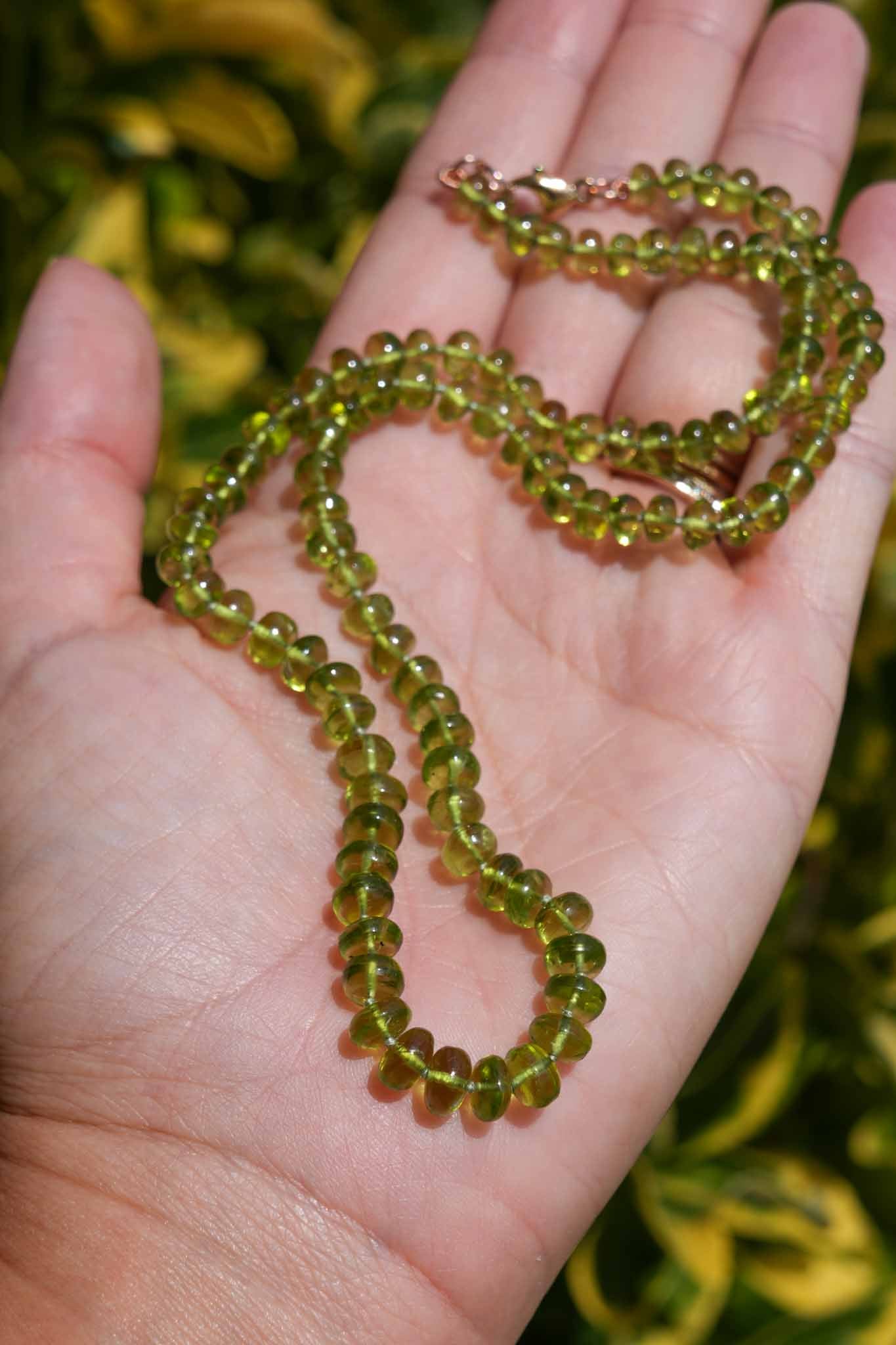 Green beaded necklace held in a hand with a blurred green background