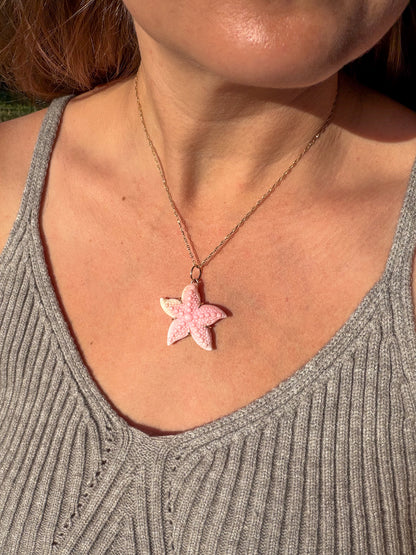 Person wearing a necklace with a pink starfish pendant.