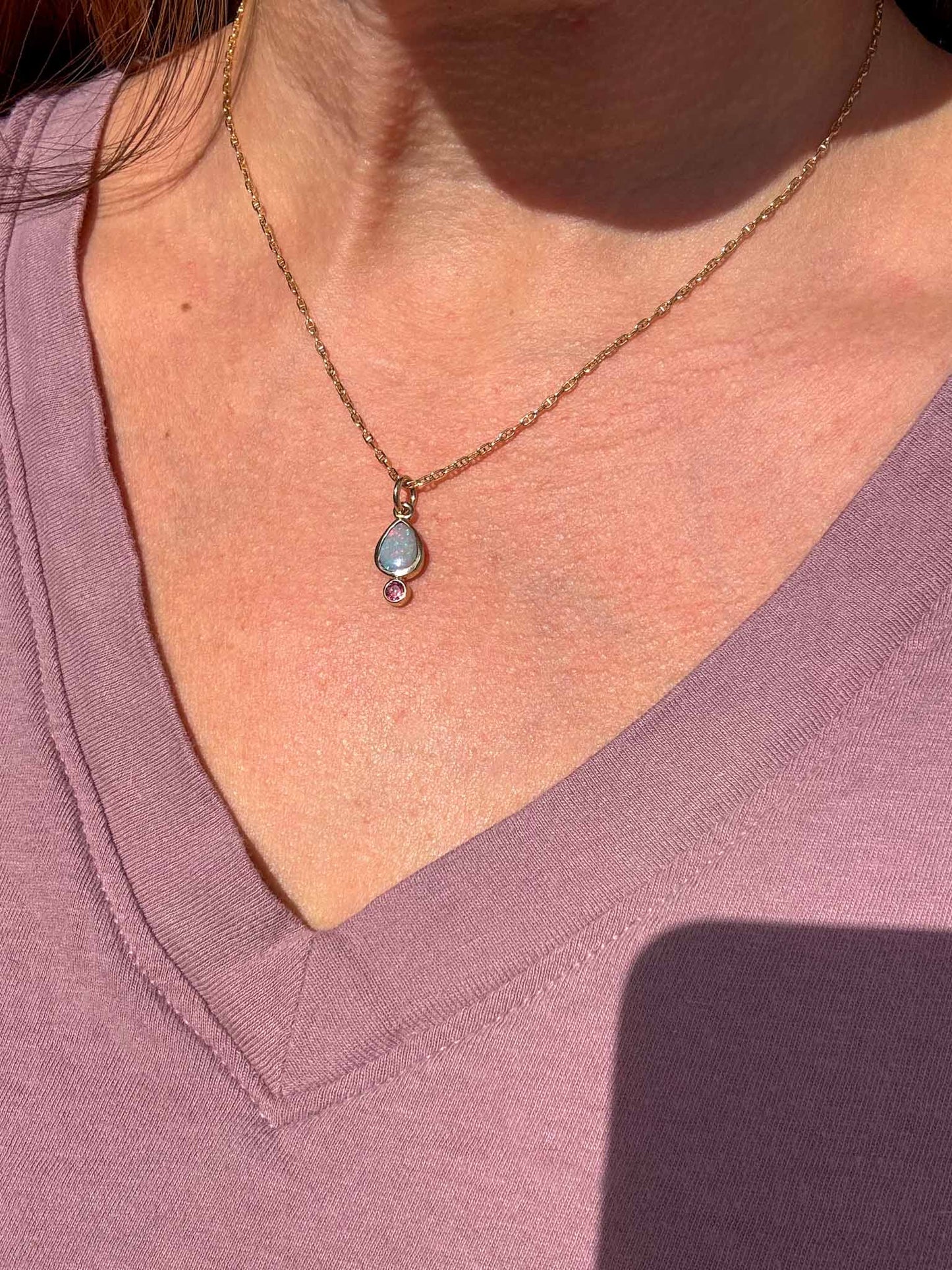 Necklace with a pendant worn by a person in a purple shirt.