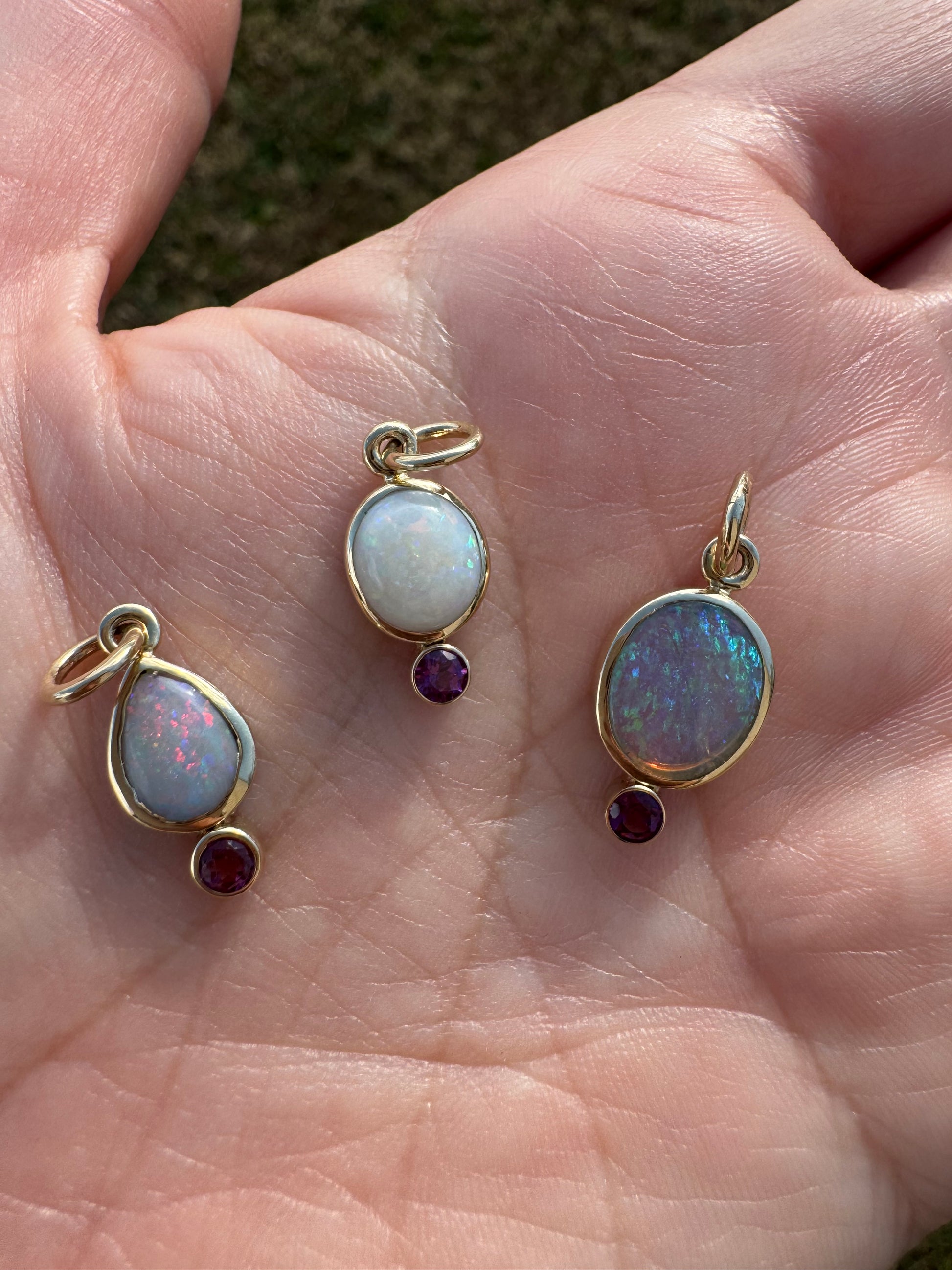 Three gold australian opal pendants with gemstones held in a hand.