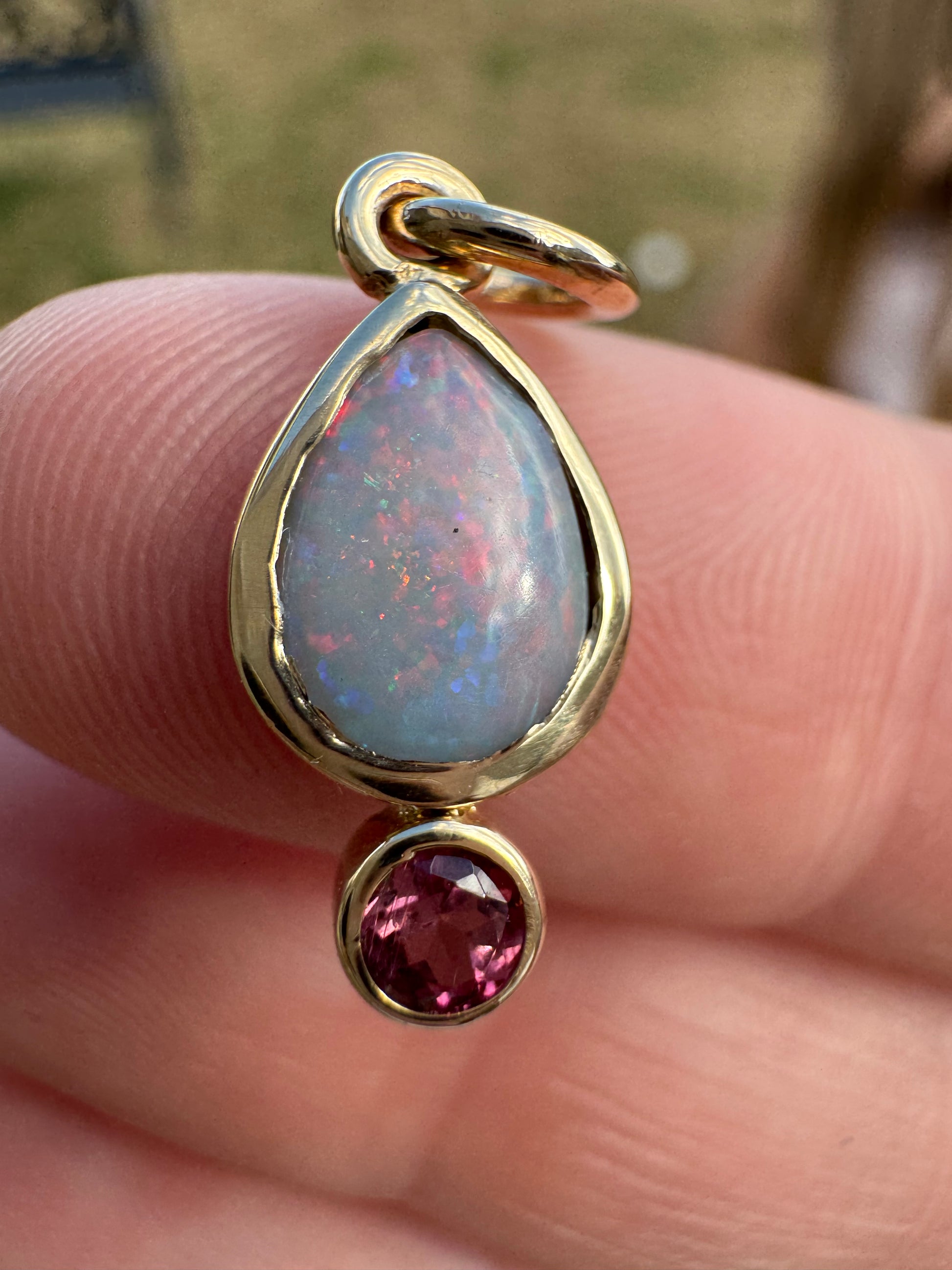 Gold charm with opal and red gemstone held between fingers