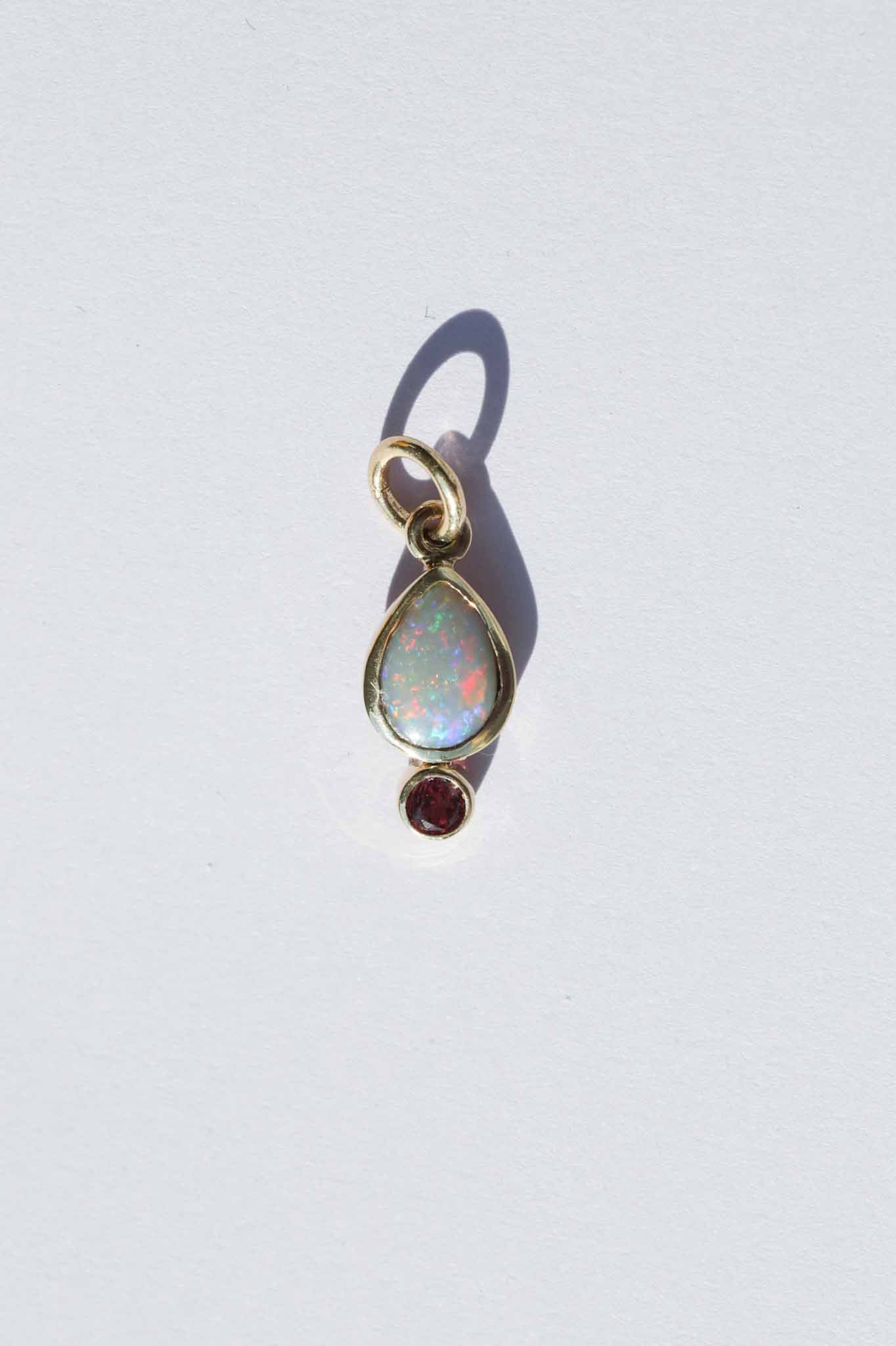Gold pendant with opal and red gemstone on a white background