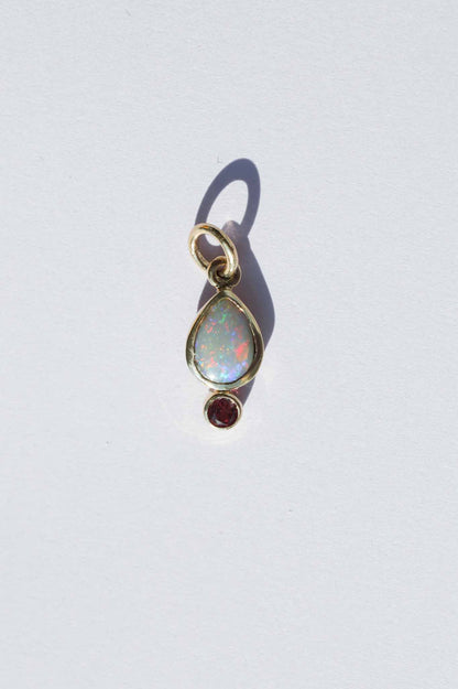 Gold pendant with opal and red gemstone on a white background
