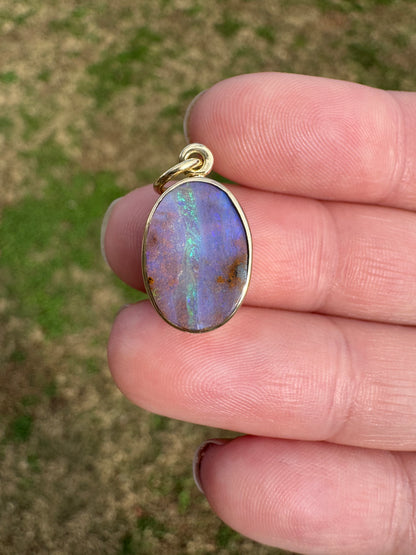 Opal pendant held between fingers with a blurred natural background