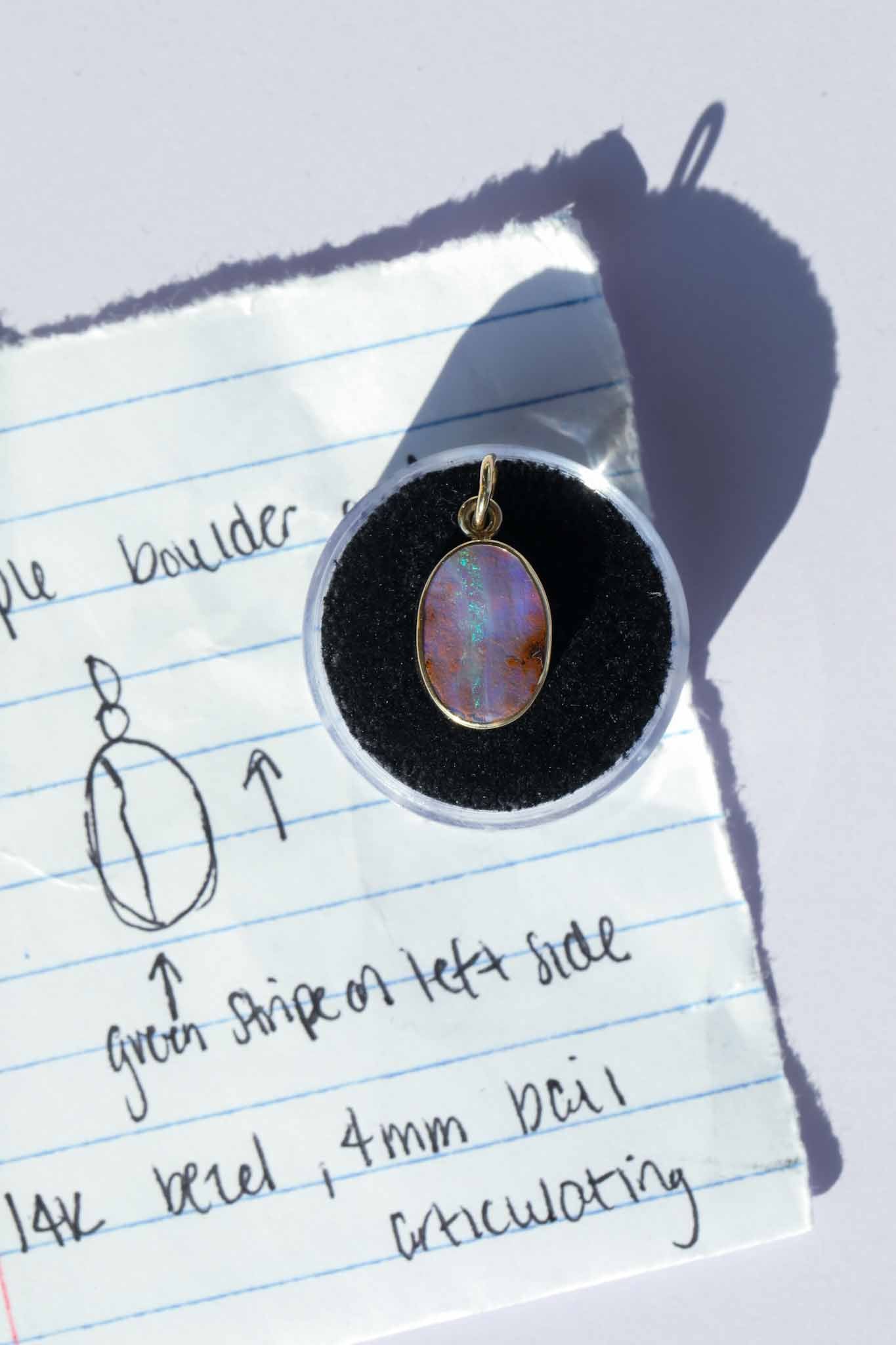 Opal pendant on a black cushion against a piece of lined paper with notes.