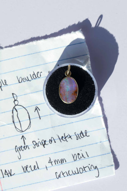 Opal pendant on a black cushion against a piece of lined paper with notes.
