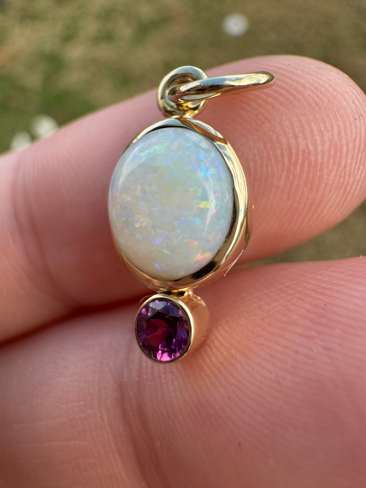 Gold charm with opal and garnet stone held between fingers
