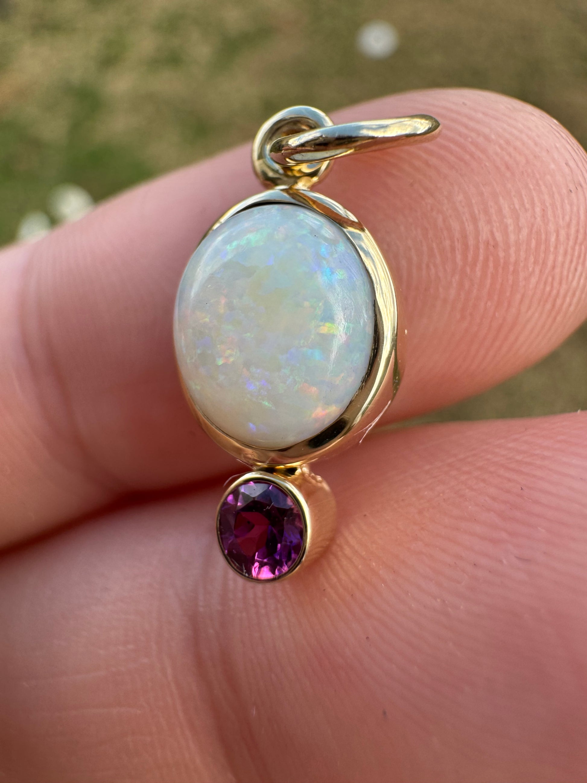 Gold charm with opal and garnet stone held between fingers