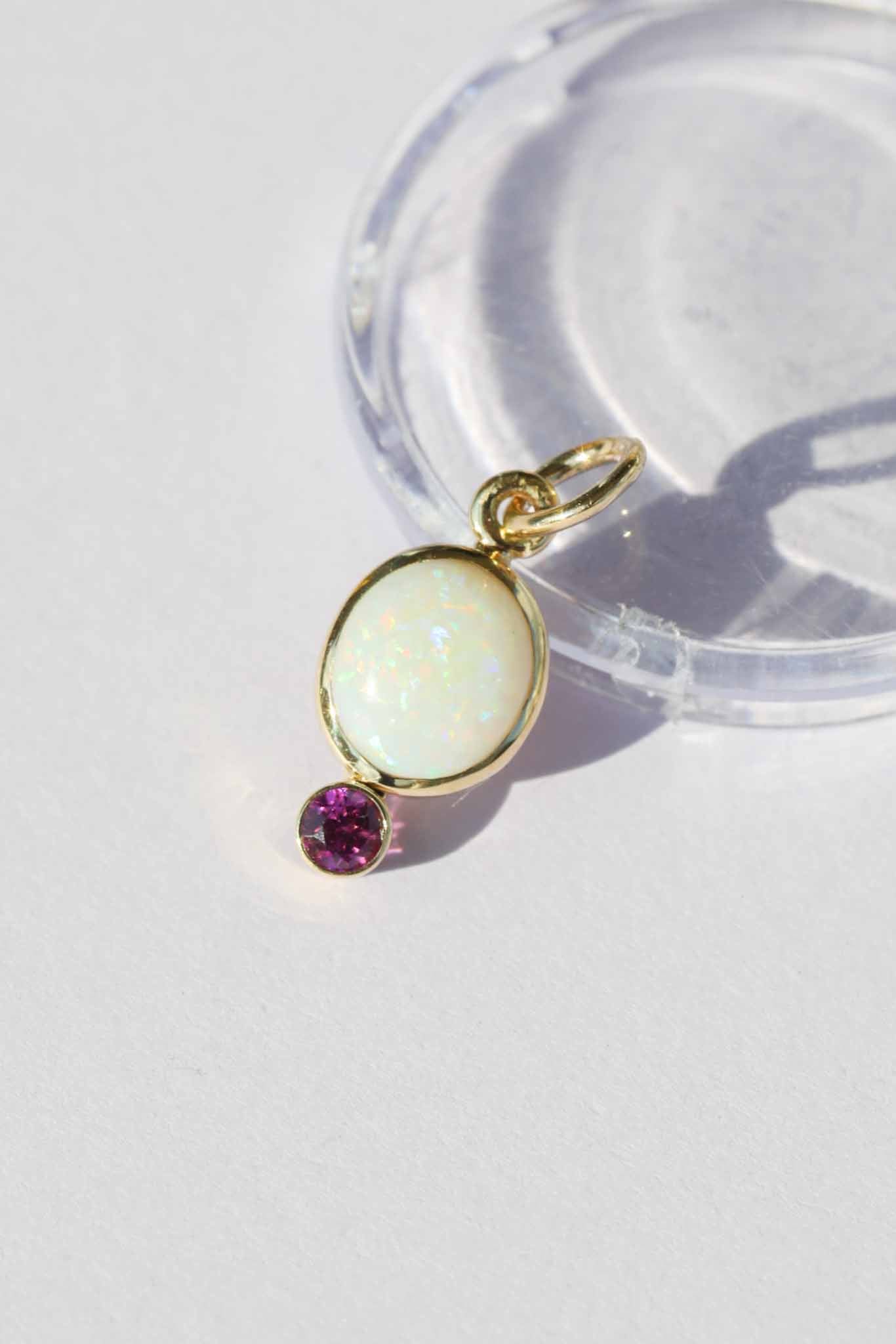 Gold pendant with a white stone and purple gem on a white background