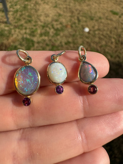 Three gold-rimmed gemstone pendants on a hand with a blurred outdoor background
