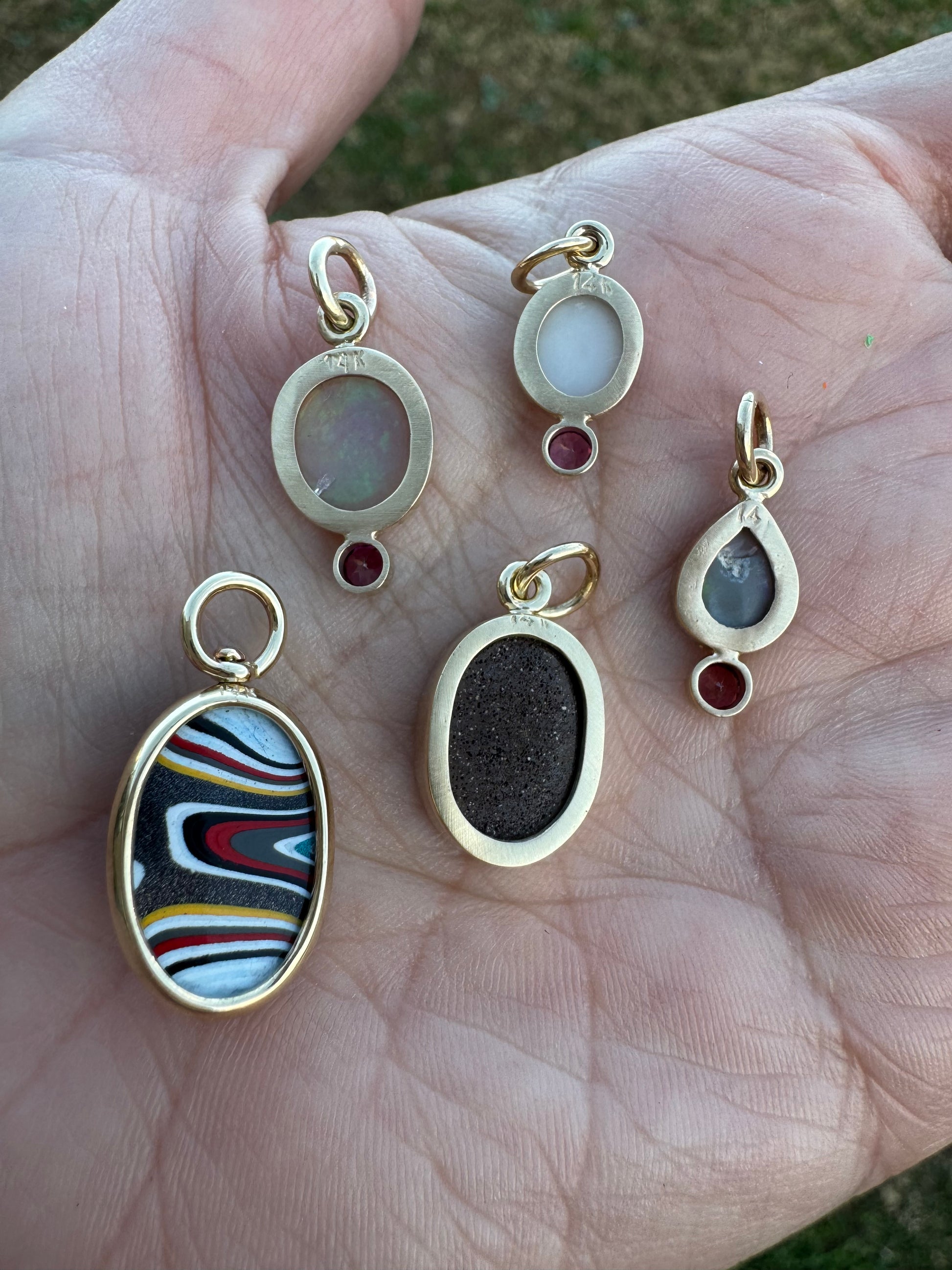 Gold pendants with various colored stones held in a hand.