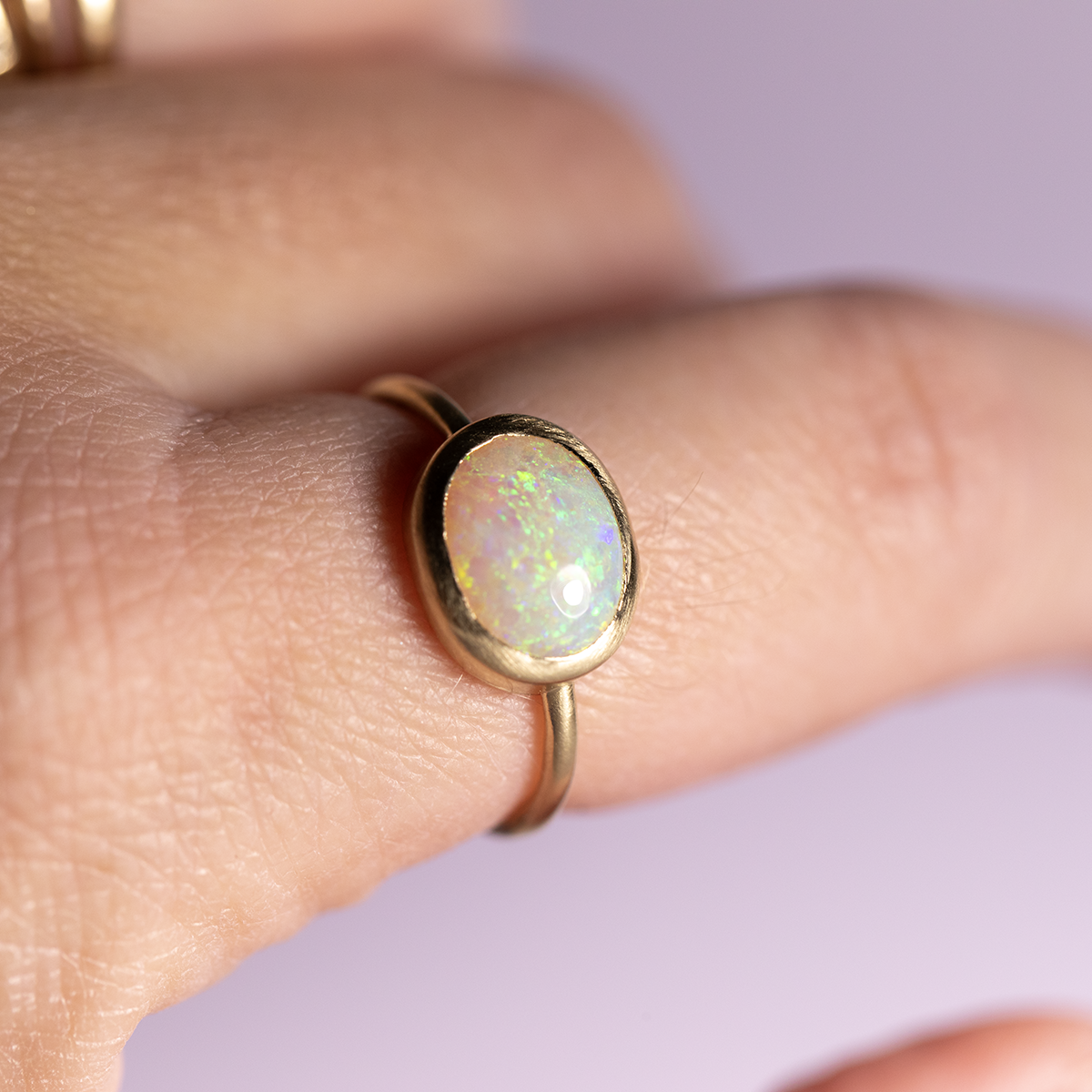 Gold ring with an opal stone on a finger against a light purple background