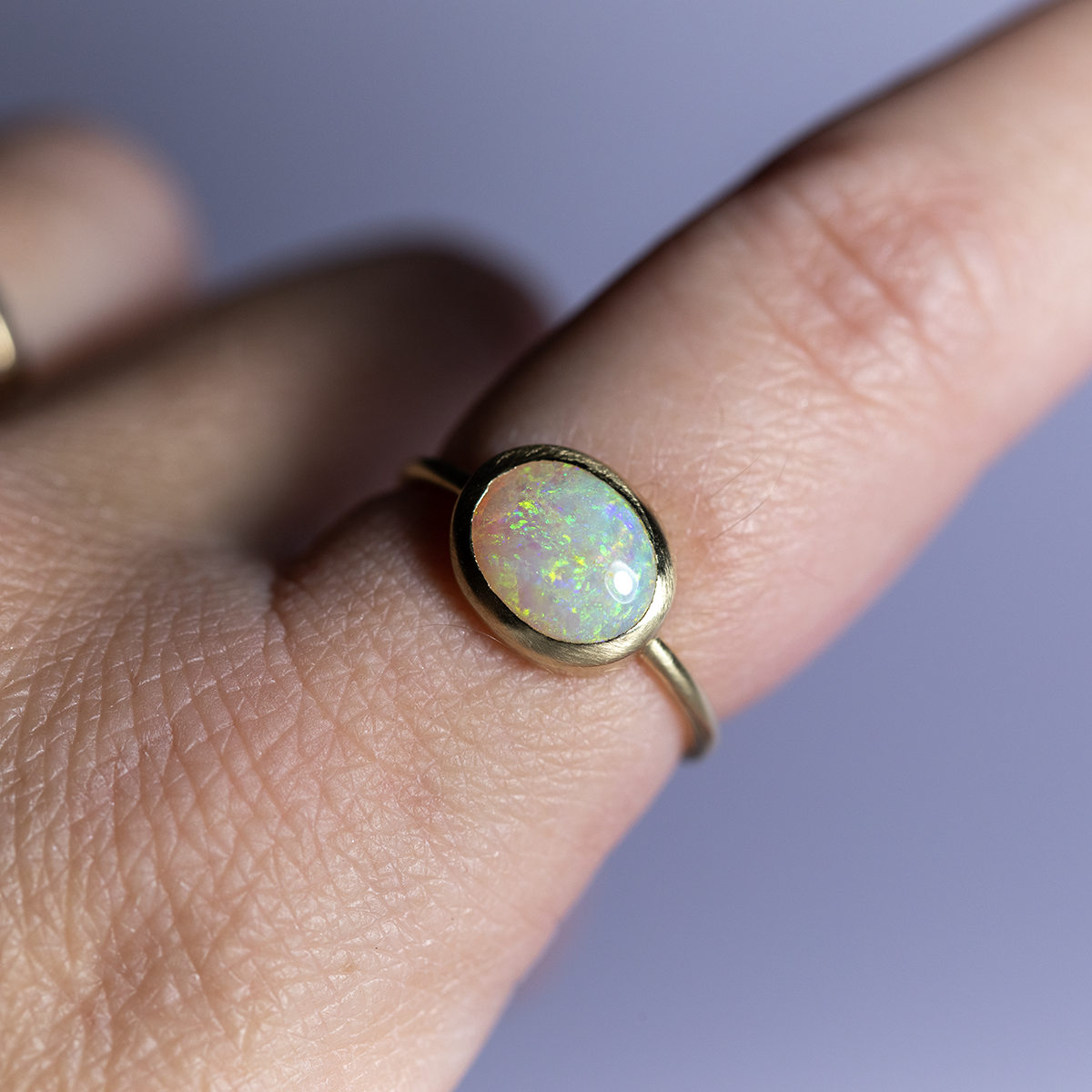 Gold ring with an opal stone on a finger against a purple background