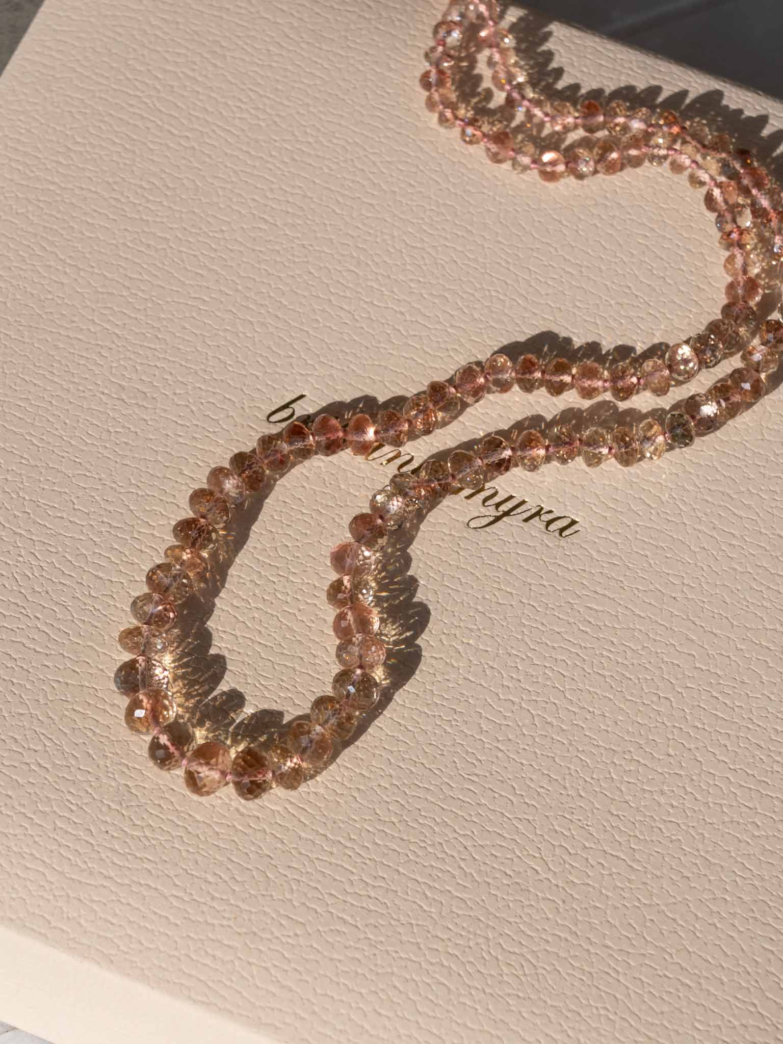 red peach pink champagne oregon sunstone rondelle beads strung together with hand tied silk knots lay on a branded brittany myra jewelry box in the sun
