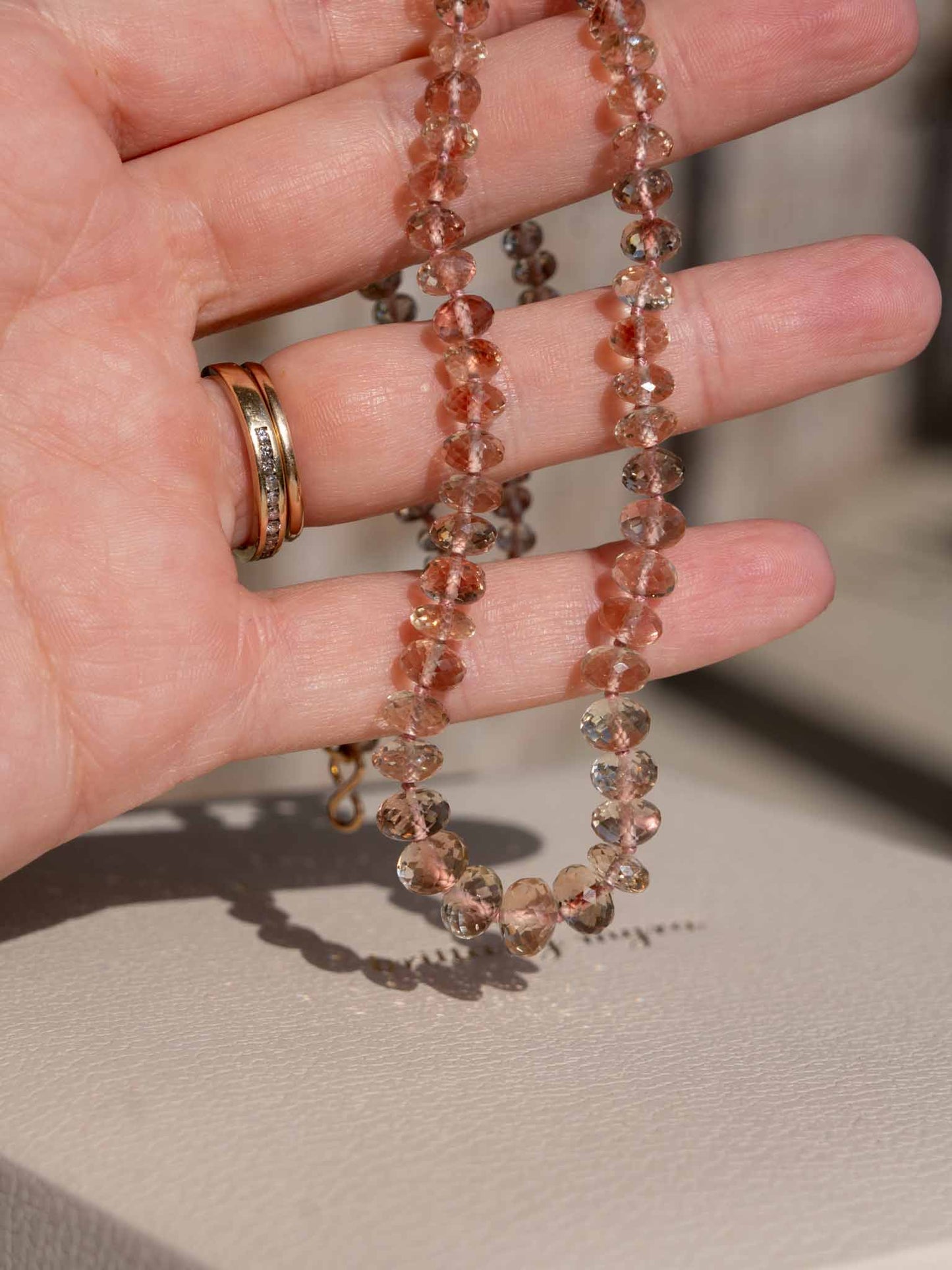 Hand holding a beaded necklace with a blurred background genuine oregon sunstone peach red schiller beaded gemstone necklace fine 14k gold jewelry minimalist necklace