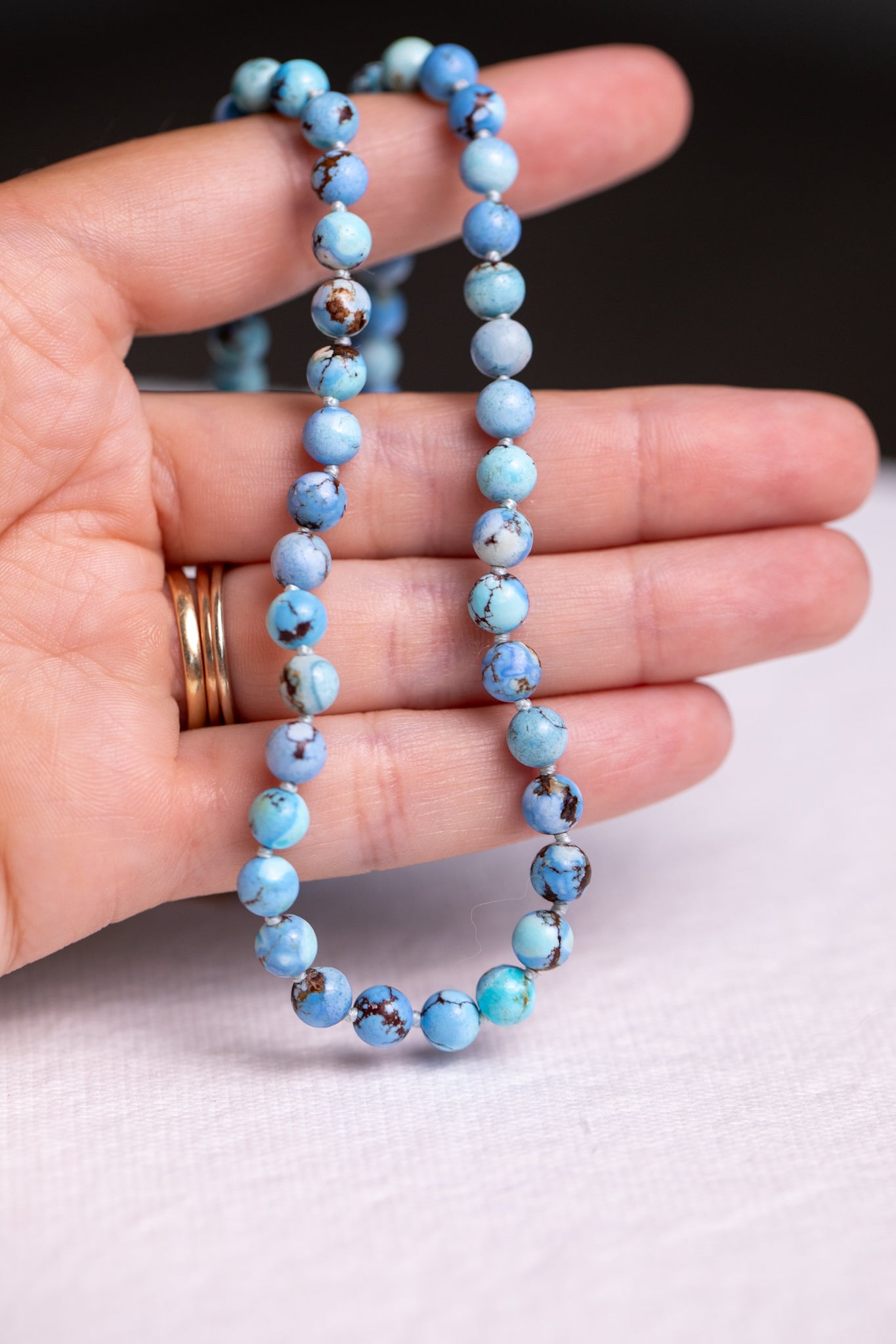 Hand holding a golden hills turquoise gemstone strand showing blue beads with brown matrix