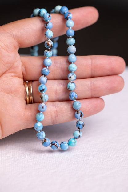 Hand holding a golden hills turquoise gemstone strand showing blue beads with brown matrix