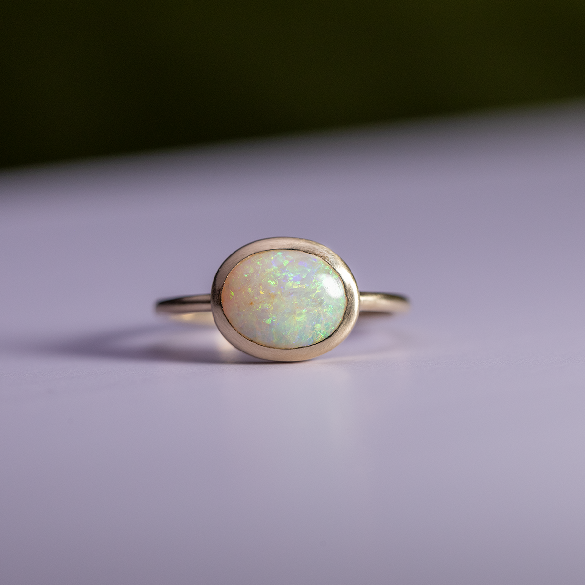 Gold ring with a greenish opal stone on a light purple background