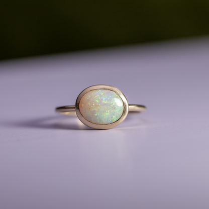 Gold ring with a greenish opal stone on a light purple background